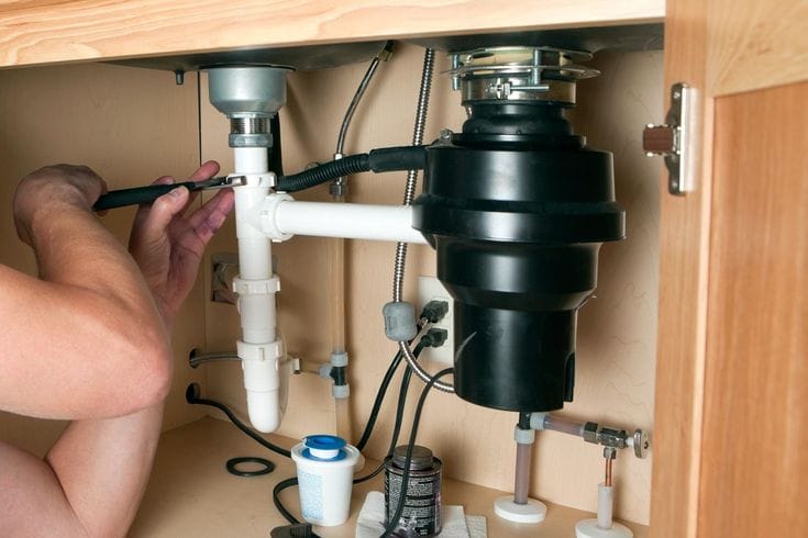 Plumber installing a garbage disposal beneath a kitchen sink in Chambersburg