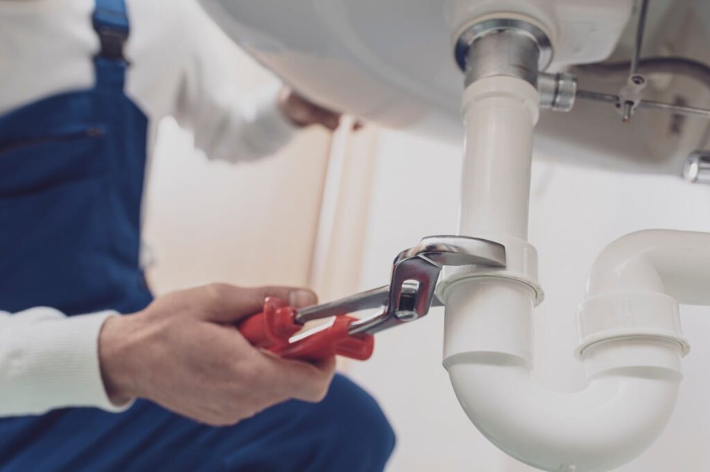 Plumber repairing a white drain pipe beneath a sink in Chambersburg